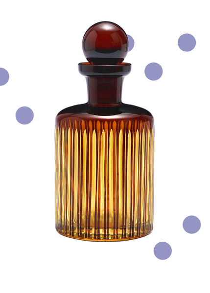 An amber glass L'Objet Prism decanter with a ribbed vertical pattern and a matching dark amber glass stopper, shown on a white background with scattered decorative purple dots.