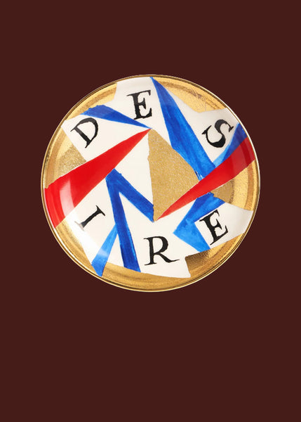 The word "Desire" is hand painted on this red, gold, blue and white hand made round ceramic plate.  The colours are organised in an abstract arrangement, with a 24 carat gold finish.