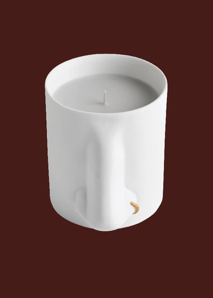 A white ceramic L'Objet candle vessel with a nose protruding from the front, shown against a solid burgundy background.